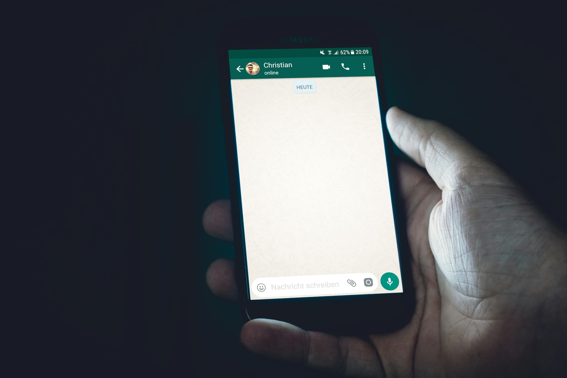 Mão segurando o celular com uma conversa de WhatsApp aberta